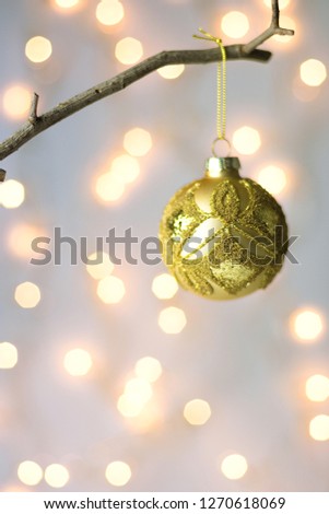 Golden ornament Christmas tree ball hanging on branch. Golden garland bokeh lights on pastel background. New Year greeting card poster with copy space