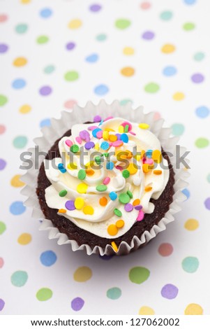 Close-up overhead shot of a cupcake decorated with colorful sprinkles over polka dots background.