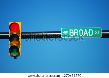 A traffic light hung on a pole above Broad street with a sign showing the street name and a blue sky background. 