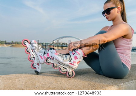 Attractive young woman putting on roller skates outdoors 