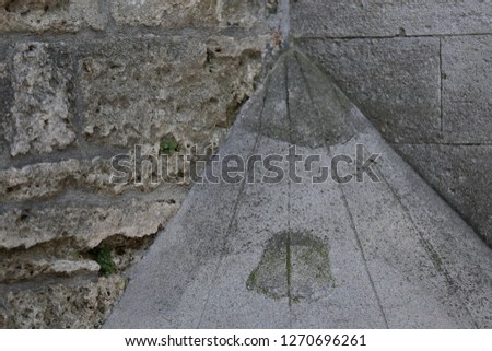 Abstract outdoor view of the base of a stone walls corner reinforced with concrete masonry. Ancient architectural element with a conical shape. Design with oblique lines and a grey rounding surface. 