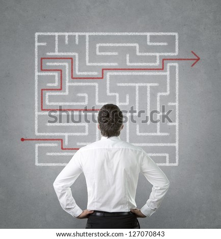 Confused, young businessman looking at the red arrow through the labyrinth