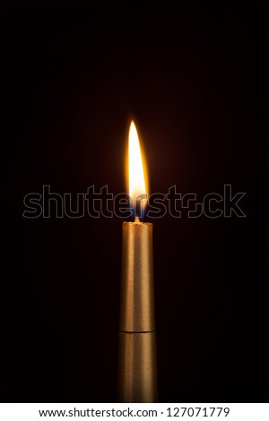 Burning golden candle against a dark background