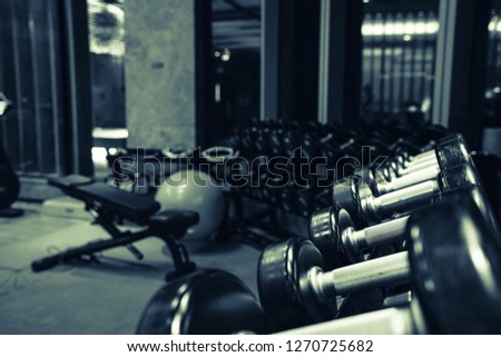 Modern light gym. Sports equipment in gym. Barbells of different weight on rack.Background blurry people in motion.