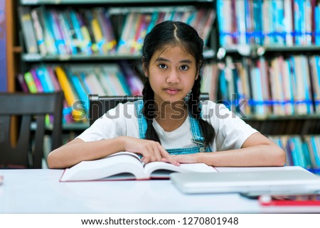School education and literacy concept with young Asian girl student.Young school girl reading a book at the library