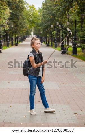 stylish modern teenager girl on a walk takes pictures of herself on a selfie stick