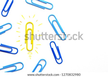 A yellow paper clip as a symbol of a light bulb that radiates lies on a white surface and symbolized the brainstorming - next to it are other paper clips without illusion
