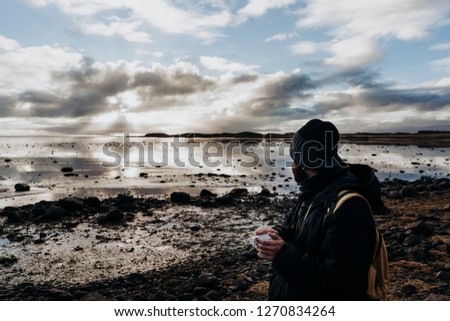 Anonymous tourist with cup of coffee against lake in Iceland
