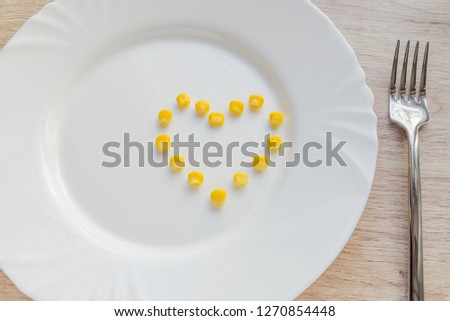 Close up of sweet corn in shape of heart and steel fork on white plate.