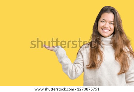 Young beautiful brunette woman wearing turtleneck sweater over isolated background smiling cheerful presenting and pointing with palm of hand looking at the camera.