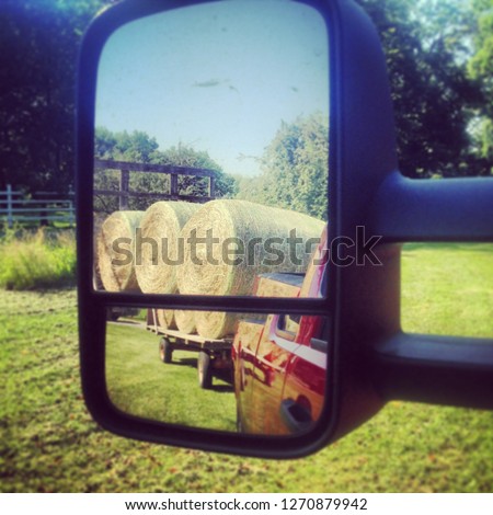 Rear view mirror of red truck showing round bales of hay on organic Wisconsin family farm 