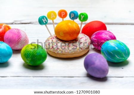 very colorful, brightly painted eggs next to a colorful donut with the word HAPPY