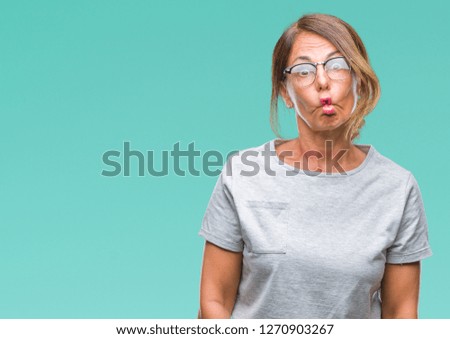 Middle age senior hispanic woman wearing glasses over isolated background making fish face with lips, crazy and comical gesture. Funny expression.
