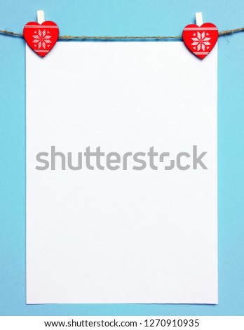 Two red hearts hold a sheet of paper for congratulations on a blue background. Valentine's day background with hearts for a greeting card.