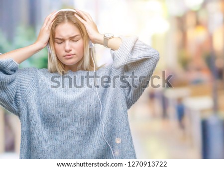 Young caucasian woman listening to music wearing headphones over isolated background suffering from headache desperate and stressed because pain and migraine. Hands on head.