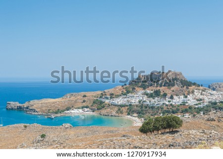 Distant view at Lindos Town and Castle with ancient ruins of the Acropolis on sunny warm day. Island of Rhodes, Greece. Europe.