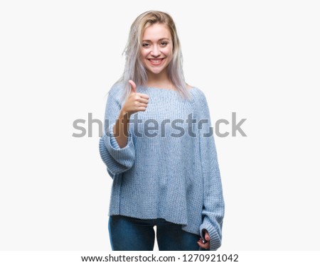 Young blonde woman wearing winter sweater over isolated background doing happy thumbs up gesture with hand. Approving expression looking at the camera with showing success.