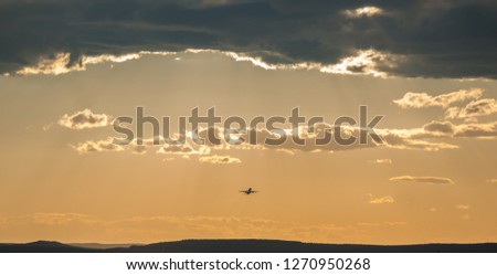 Beautiful dramatic gray cloud on orange sunset sky. Small silhouette of an airplane in the distance rising upward the clouds after takeoff. Air transport, natural colorful texture sky background.