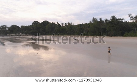 Aerial for man jogging on a tropical sandy beach near the sea. Shot. Beautiful aerial view of a runner man training on the beach.