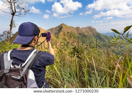 Young hiker taking a photography along path of terkking. Photographer taking photo at mountain peak.