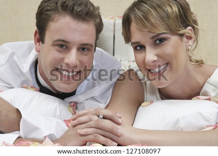 Portrait of a happy newlywed couple lying in bed while holding hands