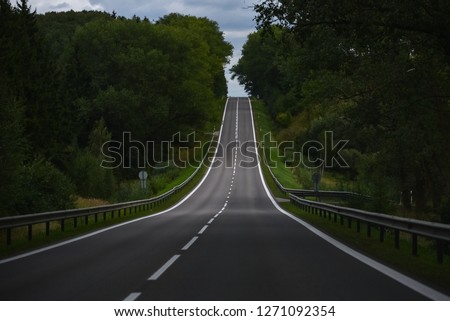 Driving uphill on the straight asphalt road surrounded by big trees. Royalty-Free Stock Photo #1271092354