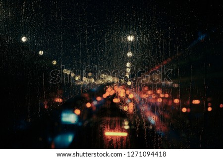 Abstract night city light and bokeh through car windscreen covered in rain, defocussed background.