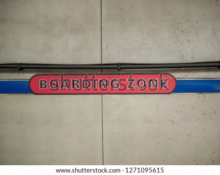 Red boarding zone sign on concrete wall in underground subway station