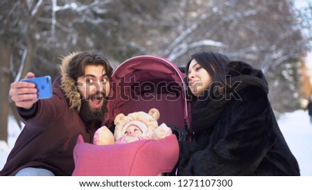 Couple with baby take selfie on walk. Young married couple with baby in pram take selfie on walk in winter. Modern young happy family