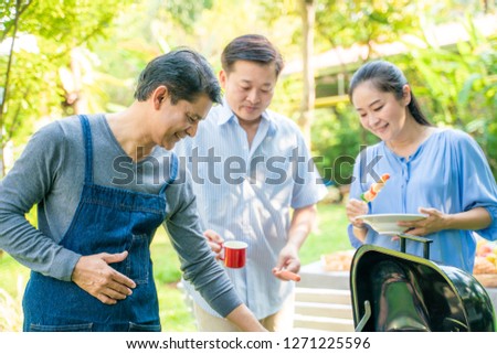 Group of mature middle aged have picnic party in green park cooking BBQ