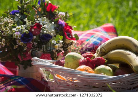 Picnic at the park on the grass: red tablecloth, basket of fruits and berries and bouquet of flowers