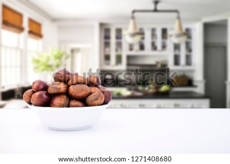 Chestnuts with modern kitchen concept idea photo. Chestnuts are in clean white porcelain plate and they are on the white table. Background is kitchen.