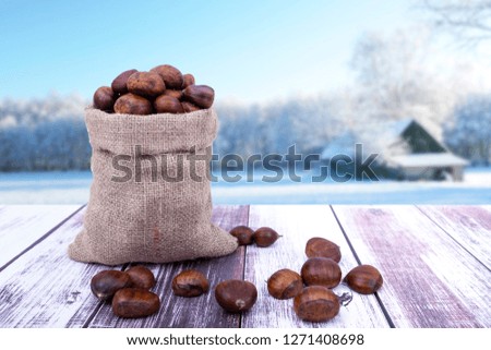 Chestnuts and winter concept idea photo. Chestnuts are in burlap jute sack bag and they are on the wooden table. Background is winter.