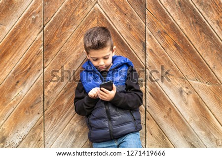Little boy with a mibile phone with a wooden door background