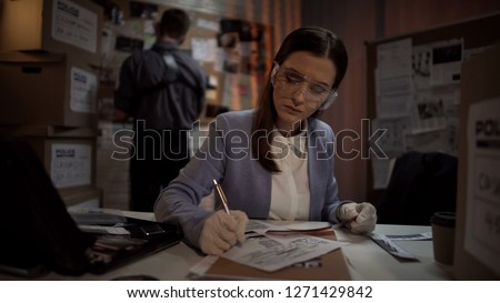 Experienced scientist looking at criminal scene photos, drawing conclusions Royalty-Free Stock Photo #1271429842