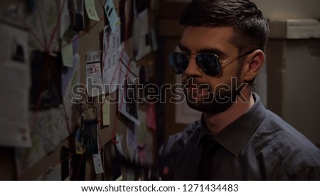 Policeman in sunglasses thinking over investigation case, board with clues