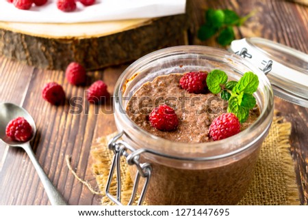 Raw Chia chocolate pudding with raspberries and mint leaves in a glass jar on a wooden table. Food photography. Stock photo