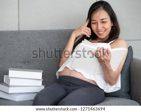 Beautiful young asian pregnant woman reading a book while lying on sofa at home