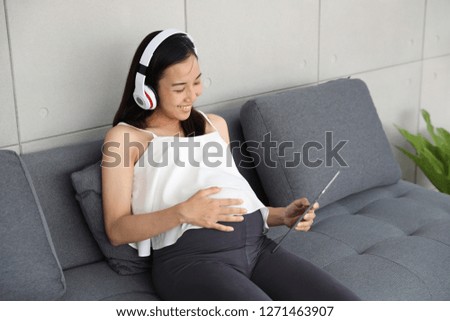 portrait of beautiful pregnant woman holding tablet and listening to music on sofa in living room 
