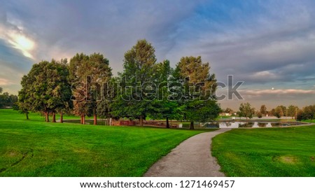 sun shining on trees at sunrise with path leading to lake with moon visible