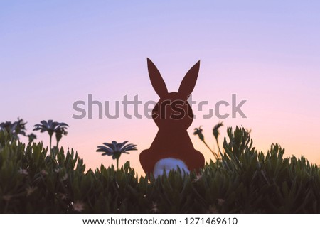 Creative easter photo of silhouette  paper rabbit in the chamomile flowers and green grass on the sunset sky background. Concept 