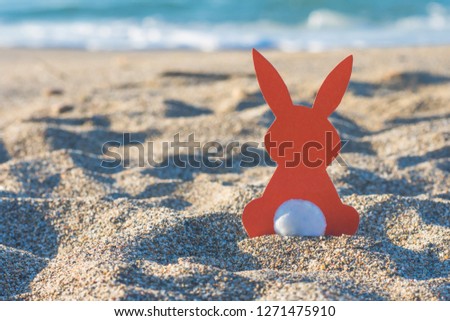 Creative easter concept photo of red paper bunny on the sand on the beach at sunset. Concept. Easter celebrations in tropical countries. 