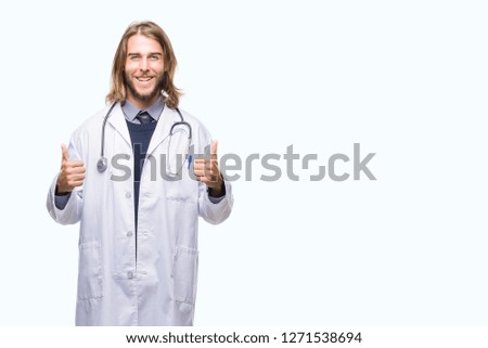 Young handsome doctor man with long hair over isolated background success sign doing positive gesture with hand, thumbs up smiling and happy. Looking at the camera with cheerful expression, winner 