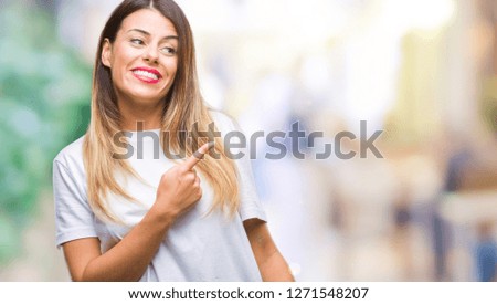 Young beautiful woman casual white t-shirt over isolated background cheerful with a smile of face pointing with hand and finger up to the side with happy and natural expression on face