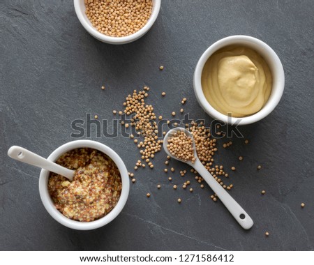 top view of jars with two kinds of mustard and whole mustard seeds on a slate plate, condiment, ingredient Royalty-Free Stock Photo #1271586412