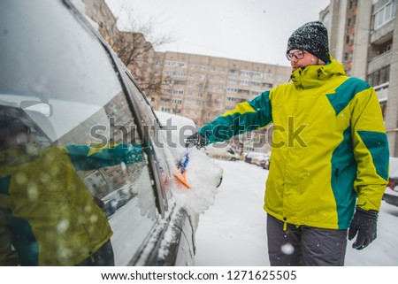 man cleaning his car after snow storm. winter time