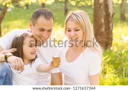 Close-up image of a young happy family spending their weekend in the park where the daughter feeding her father with the ice-cream