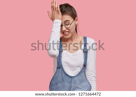 Photo of dissatisfied young woman regrets wrong doing, keeps hand on forehead, clenches teeth, dressed in fashionable outfit, isolated over pink studio wall. Lady forgets something important Royalty-Free Stock Photo #1271664472