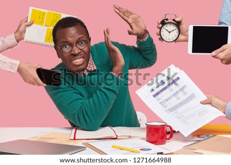 Troubled displeased dark skinned man refuses working, makes stop gesture, different people hold alarm clock, touchpad, documentation, mobile phone and spiral notebook with stickers. Dont bother! Royalty-Free Stock Photo #1271664988