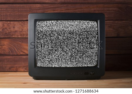 Old vintage TV set televisor on wooden table againt dark wooden wall background with no signal television grainy noise effect on the screen